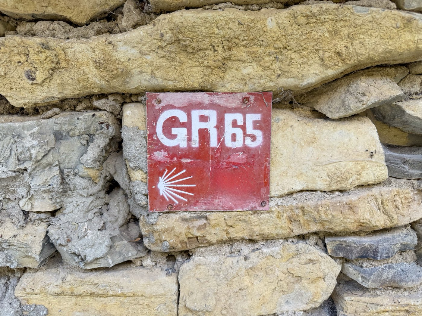 Rotes Wegzeichen mit weißer Jakobsmuschel an einer Natursteinmauer