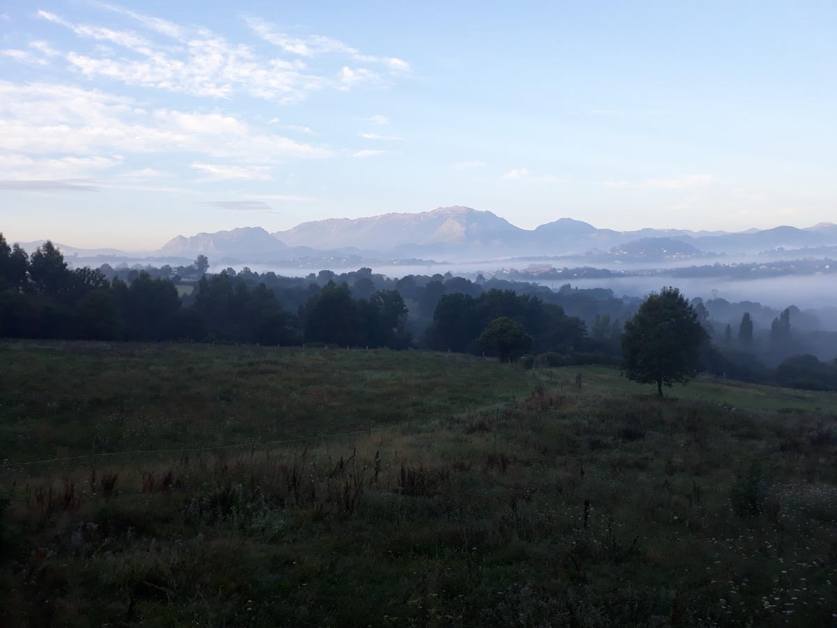 Morgennebel liegt in einem Tal am Camino Primitivo, dahinter Berge im ersten Licht