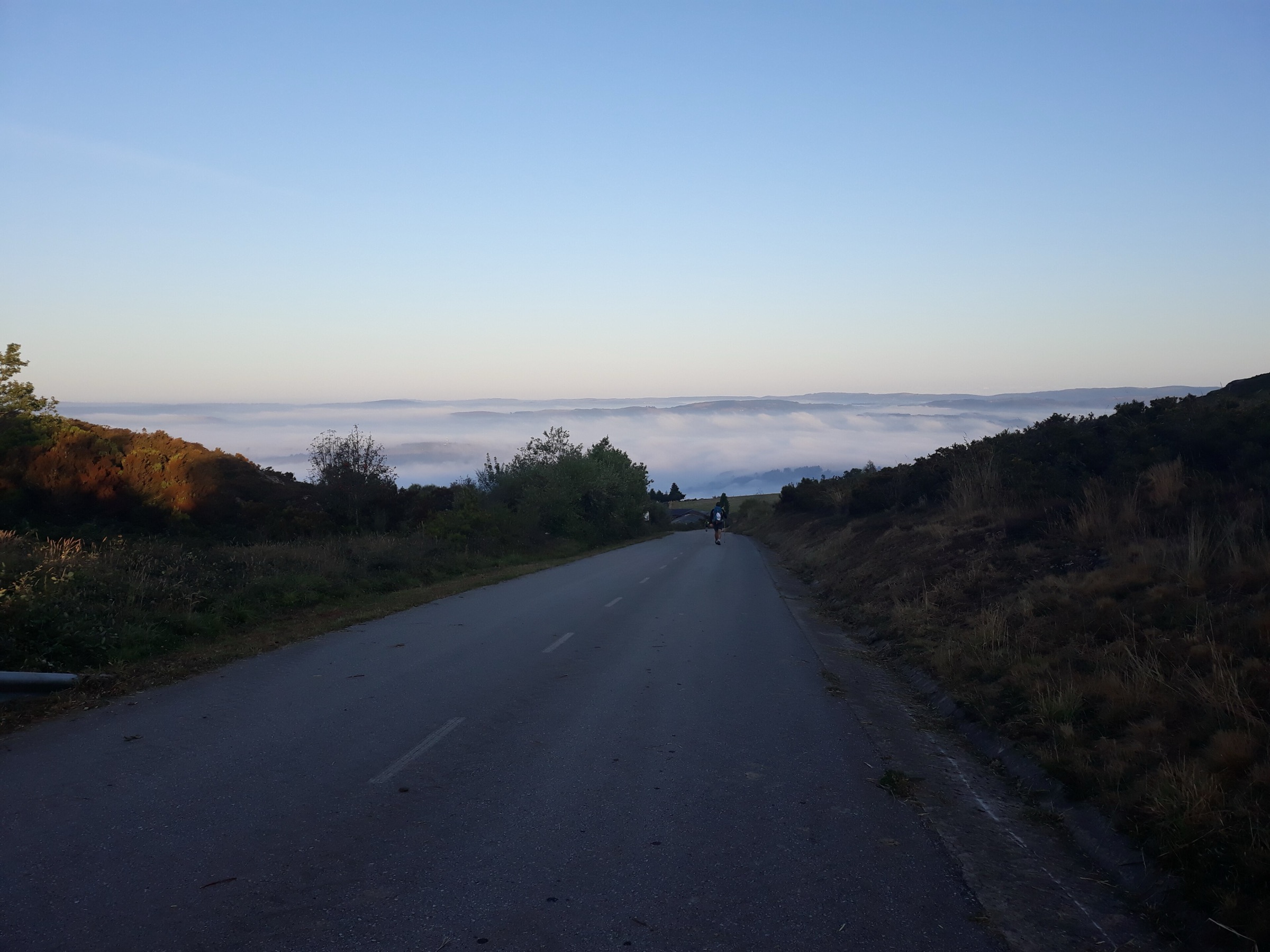 Ein Pilger bricht im Morgengrauen auf, vor ihm liegt ein Nebelmeer