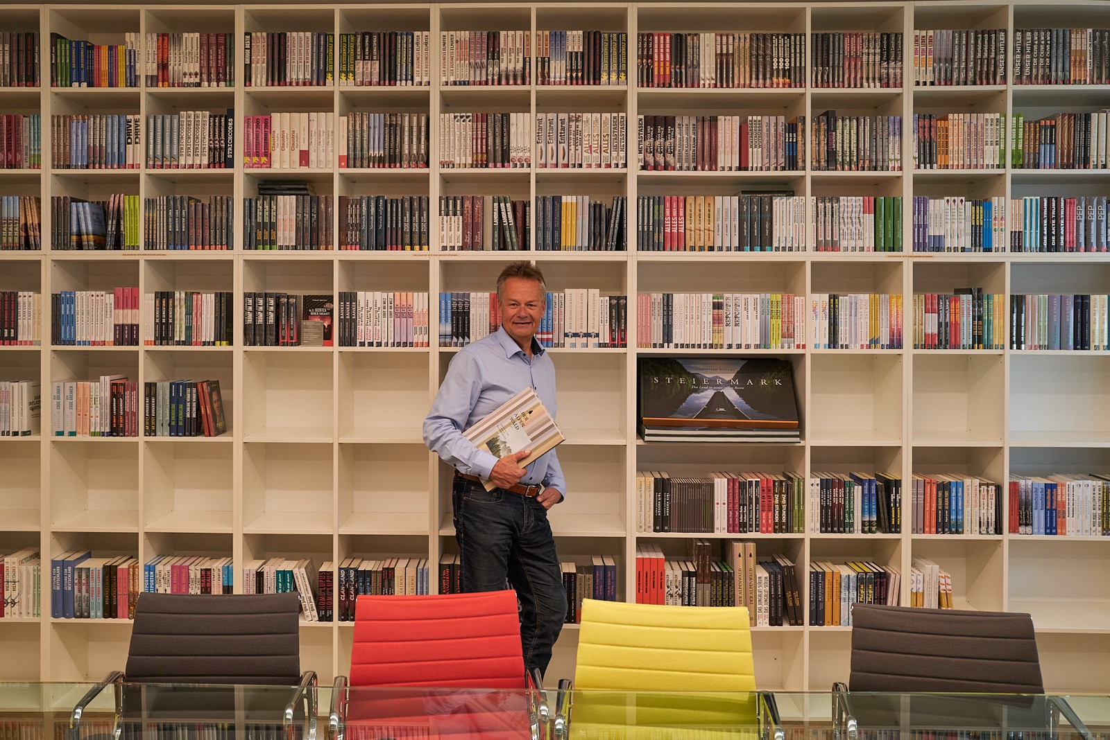 Dirk Rumberg mit einem Stapel Bücher vor einer großen Bücherwand